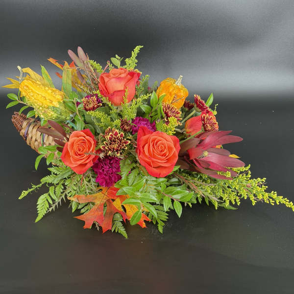 Autumn floral arrangement with orange roses and gourds in a woven basket