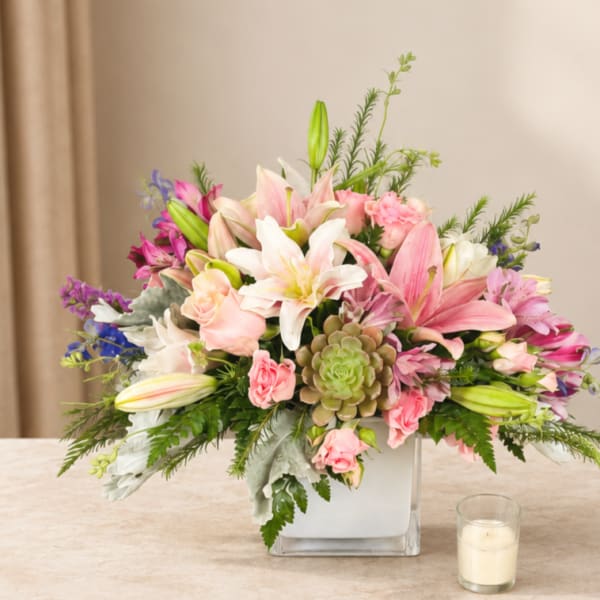 Pink and white lily bouquet in a square glass vase with a candle nearby