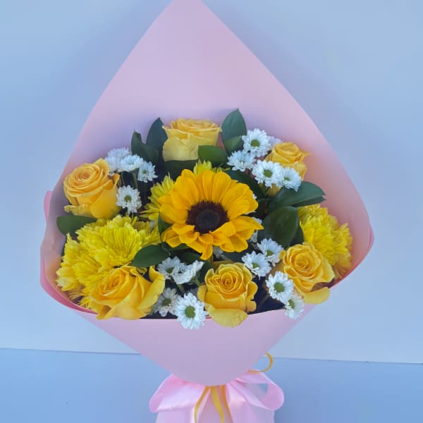 Bouquet of yellow roses, sunflowers, and white daisies wrapped in pink paper