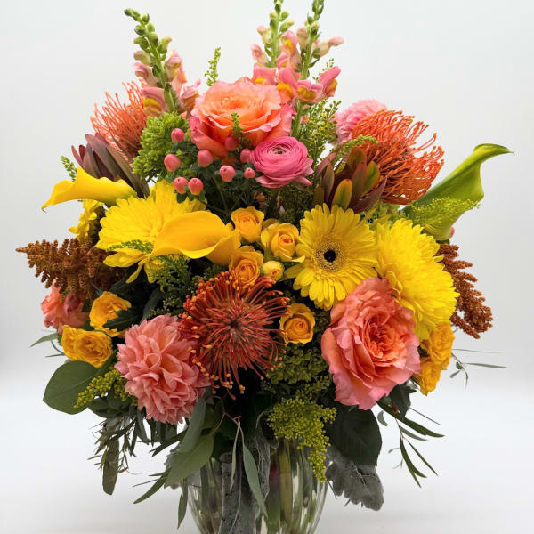 Bright mixed bouquet in a clear glass vase with pink, yellow, and orange flowers