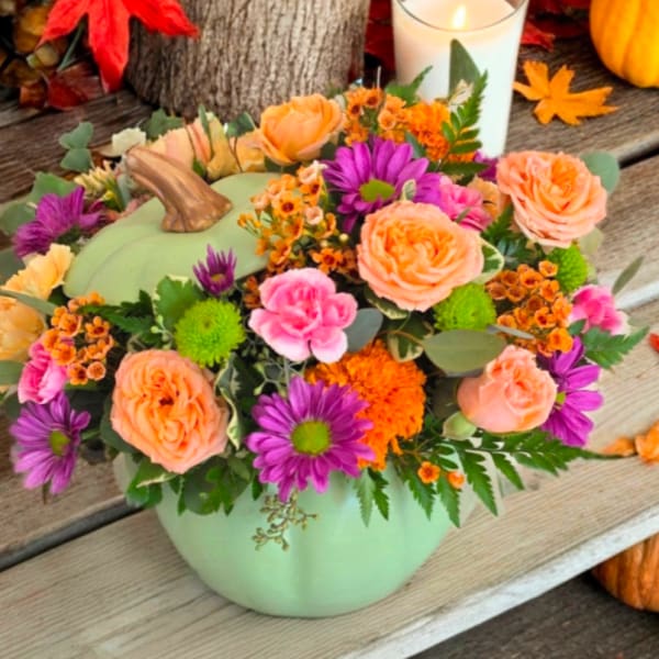 Pumpkin-shaped floral arrangement in a mint green container with peach, purple, and orange blooms