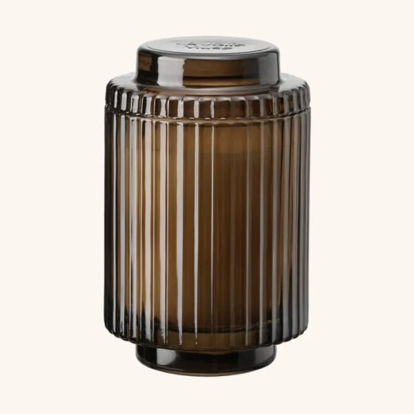 Amber ribbed glass jar with a black lid on a plain background