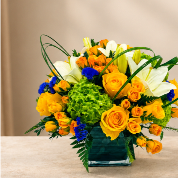 Yellow roses and white lilies in a square glass vase