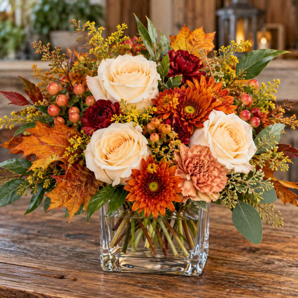 Autumn bouquet of cream roses, orange mums, and carnations in a glass vase