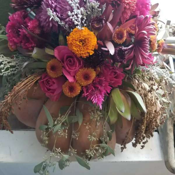 Autumn arrangement of pink roses and mixed orange and purple blooms arranged in a pumpkin container