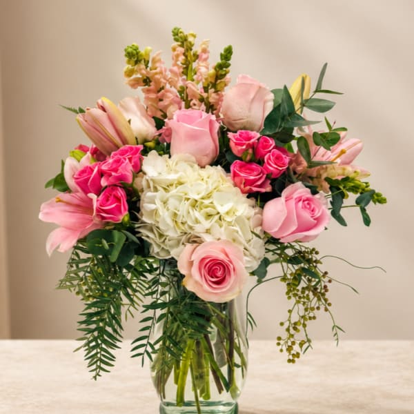 Pink roses and lilies arranged with white hydrangea in a glass vase