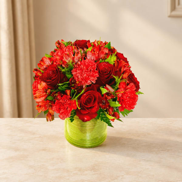 Red roses and mixed red flowers in a green glass vase