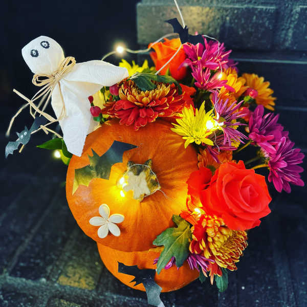 Pumpkin arrangement with colorful flowers, a ghost decoration, and bat accents