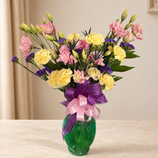 Pink and yellow flowers in a green glass vase with a purple ribbon