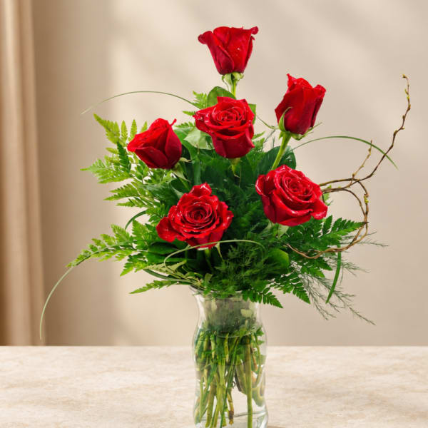 Red roses arranged in a clear glass vase with green foliage