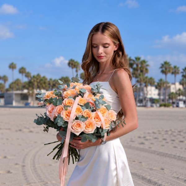 Woman in a white dress holding a bouquet of peach roses