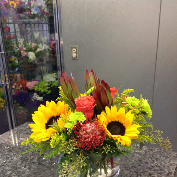Bright mixed bouquet with sunflowers, roses, and protea in a glass vase