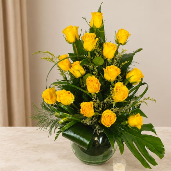 Yellow roses arranged in a glass vase with tropical greenery