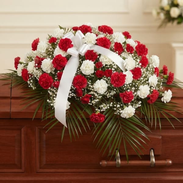 Red and white carnation casket spray with a white ribbon