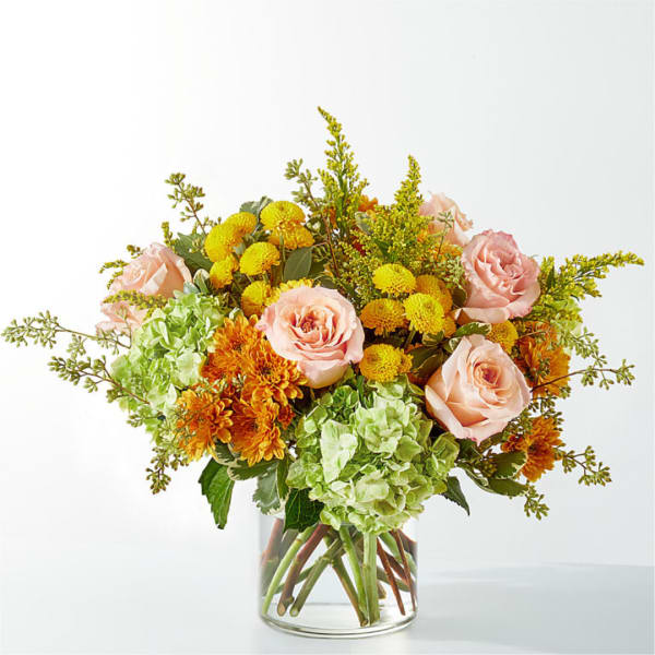 Bouquet of pink roses, green hydrangeas, and yellow-orange mums in a clear glass vase