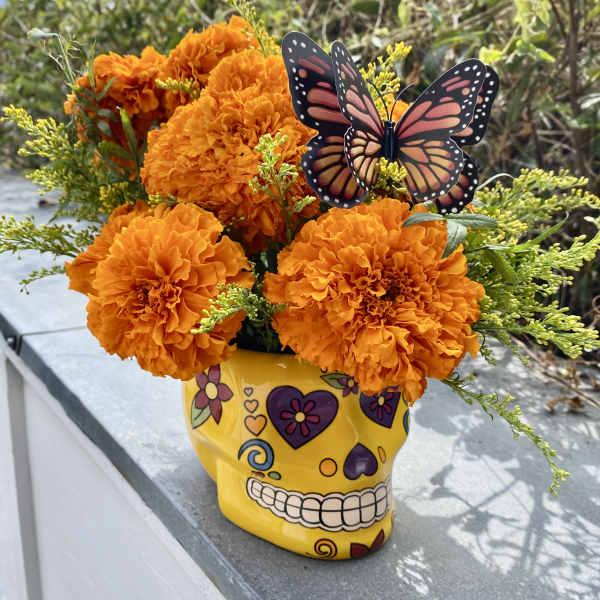 Orange marigold bouquet in a yellow skull vase with a butterfly pick