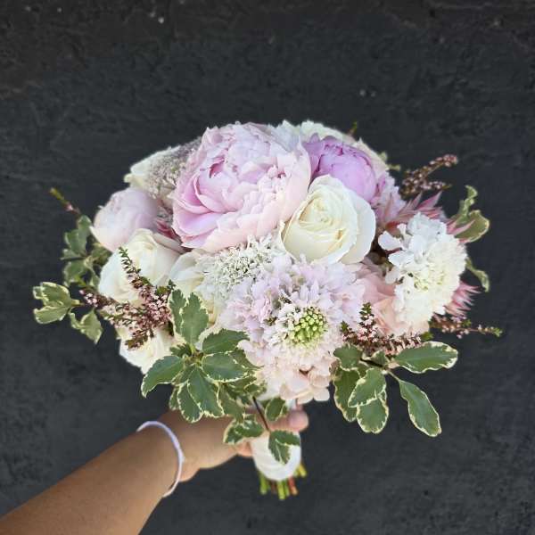 Handheld bouquet of pale pink and white flowers with variegated greenery