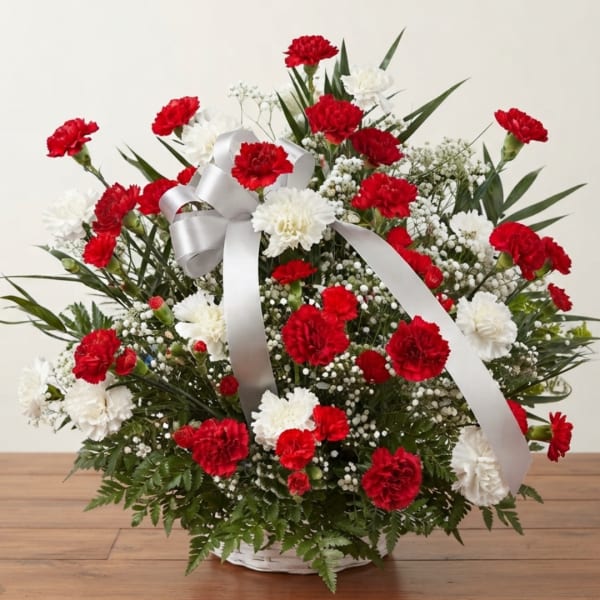 Red and white carnation arrangement in a white basket with a silver ribbon