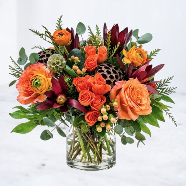 Orange roses and ranunculus in a clear glass vase