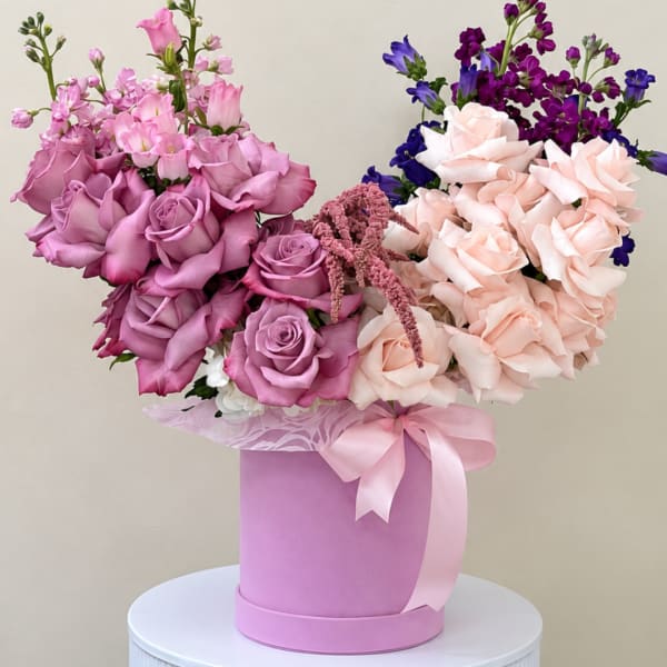 Pink and lavender roses arranged in a round hatbox with a ribbon