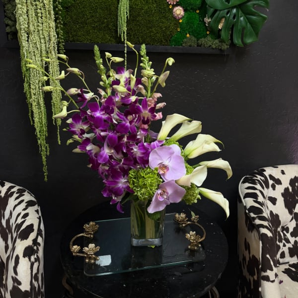 Purple orchids and white calla lilies arranged in a glass vase