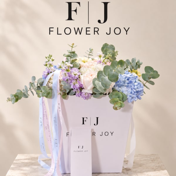 Pastel flower arrangement in a white box with ribbon streamers