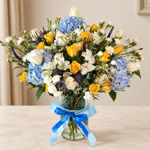 Bouquet of yellow and white roses with blue hydrangeas in a glass vase