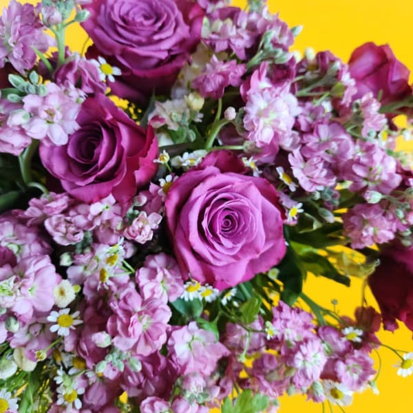 Bouquet of purple roses and pink flowers on a yellow background