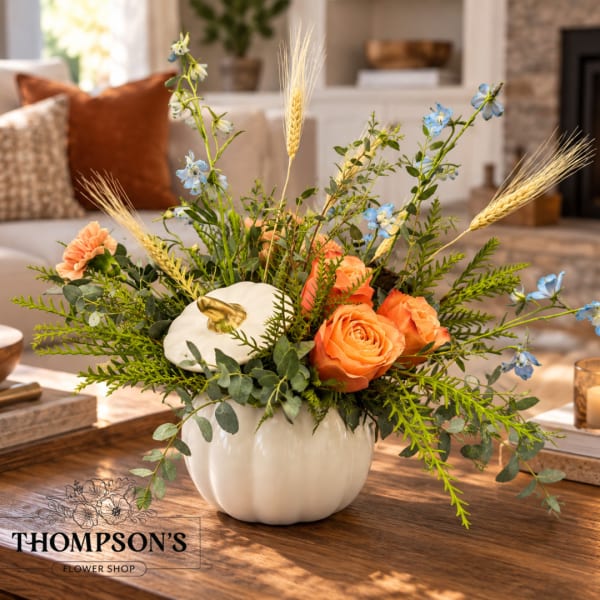 Orange roses and blue flowers arranged in a white pumpkin vase