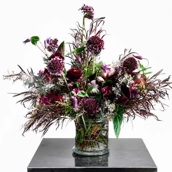 Tall burgundy and purple floral arrangement in a clear glass vase