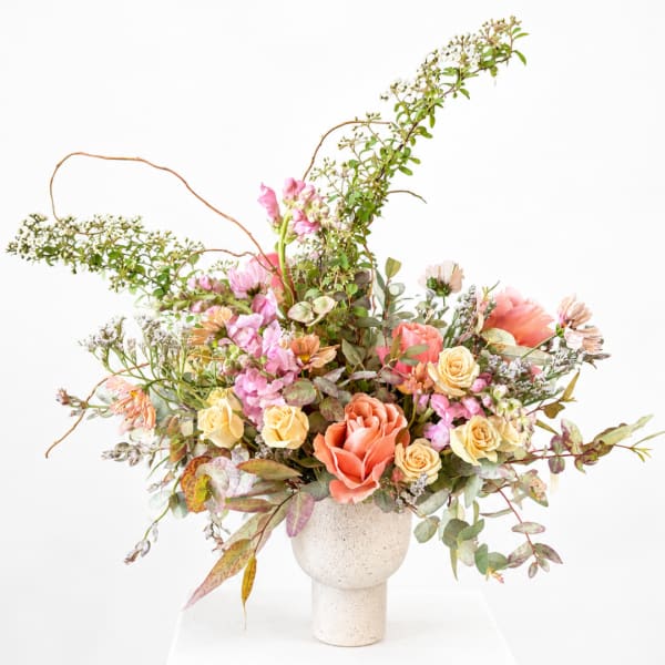 Mixed bouquet of peach, pink, and cream flowers in a speckled white vase