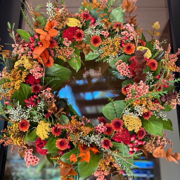 Autumn wreath with orange, red, and yellow flowers on a dark door
