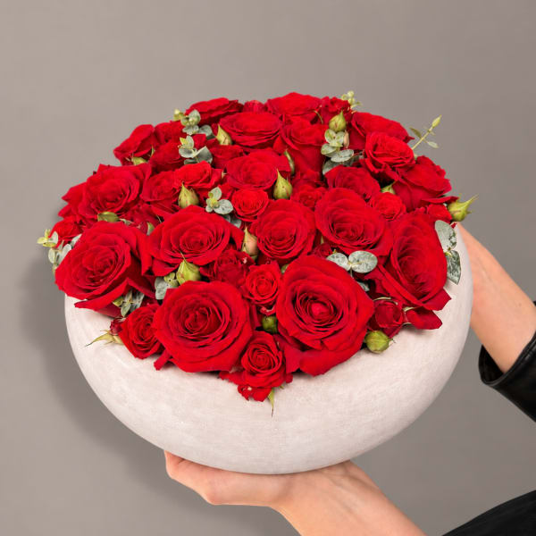 Round arrangement of red roses in a white bowl vase