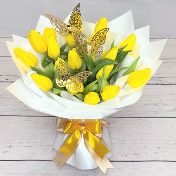 Bouquet of yellow tulips wrapped in white paper with gold butterfly picks