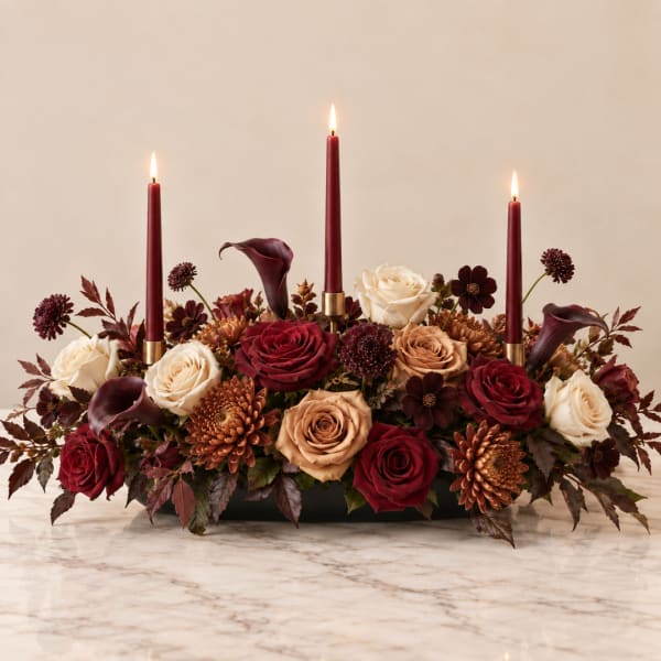 Low floral centerpiece with roses, calla lilies, and lit burgundy candles