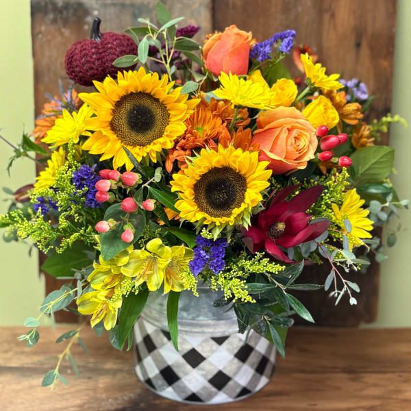 Mixed bouquet with sunflowers, roses, and colorful filler flowers in a patterned vase