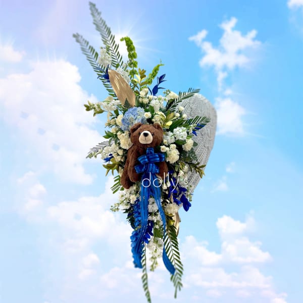 Tall floral arrangement with a teddy bear and blue ribbon against a sky background