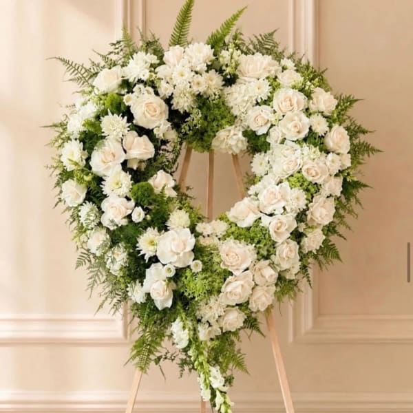 Heart-shaped white floral wreath on a wooden stand