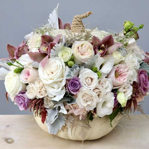 Pastel roses and orchids arranged in a white pumpkin container with a rope stem