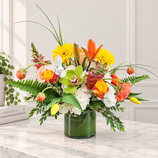 Mixed bouquet in a green glass vase with yellow, orange, white, and peach blooms