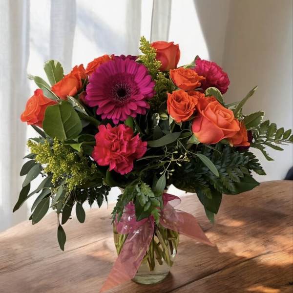 Bouquet of orange roses, pink gerbera daisies, and carnations in a glass vase