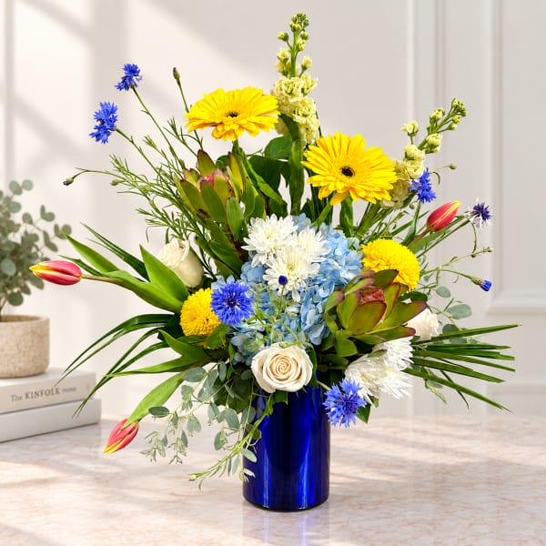 Mixed bouquet in a blue vase with yellow, white, blue, and pink flowers