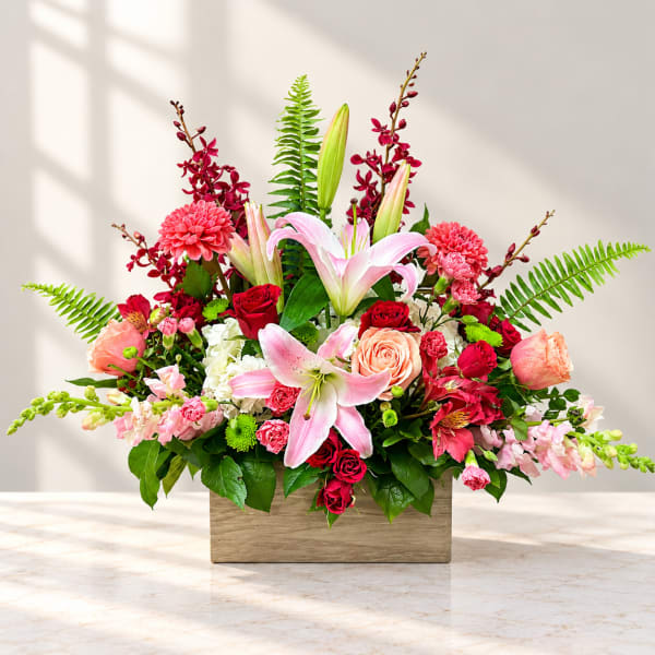 Mixed bouquet with pink lilies, roses, and red blooms in a wooden box
