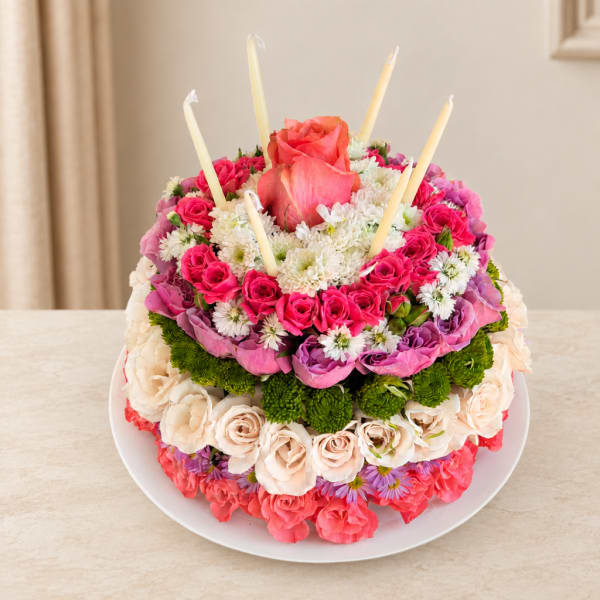 Round floral cake with pink and white roses and candles on a plate