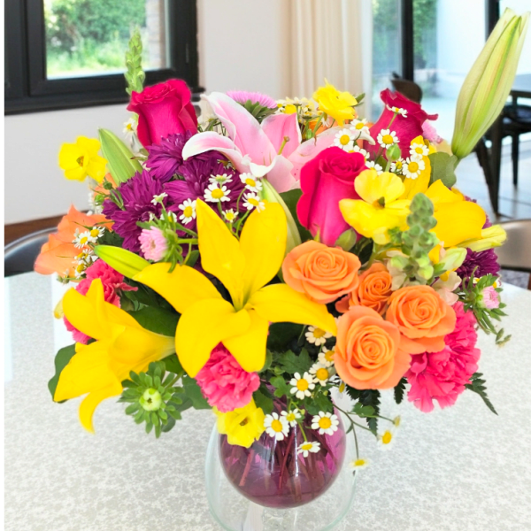 Colorful mixed bouquet in a glass vase with lilies, roses, and daisies