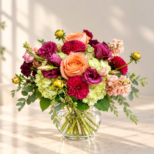 Mixed bouquet of roses, hydrangeas, and magenta blooms in a glass vase