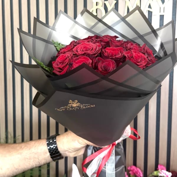 Handheld bouquet of red roses wrapped in black paper