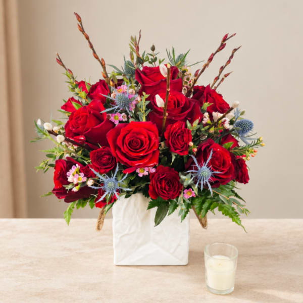 Red rose arrangement in a white square vase with small blue flowers