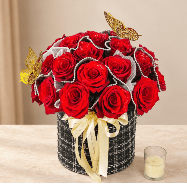 Red roses arranged in a black round box with a cream ribbon and butterfly accents