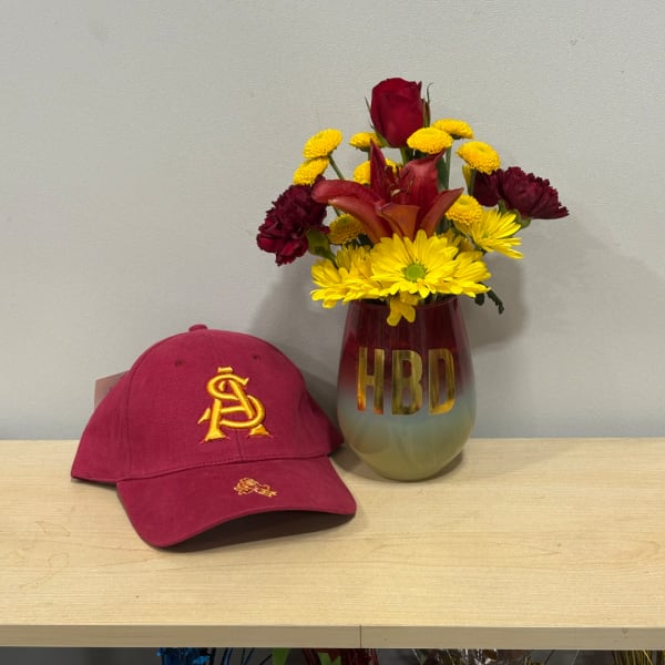 Mixed bouquet in a burgundy vase beside a maroon baseball cap